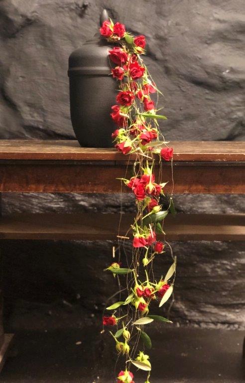 Svart urna med girlang av röda blommor