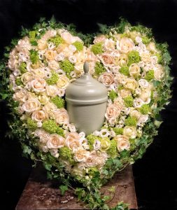 Urna mitt i ett hjärta av gula och gröna blommor