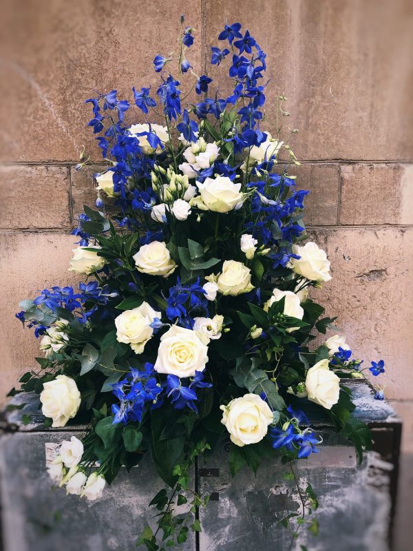 Hög dekoration mot stenvägg med blå och vita blommor