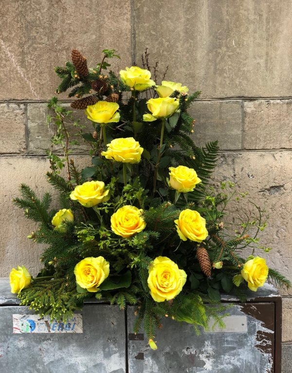 Hög dekoration med gula blommor, kottar, och barrträdskvistar från naturen